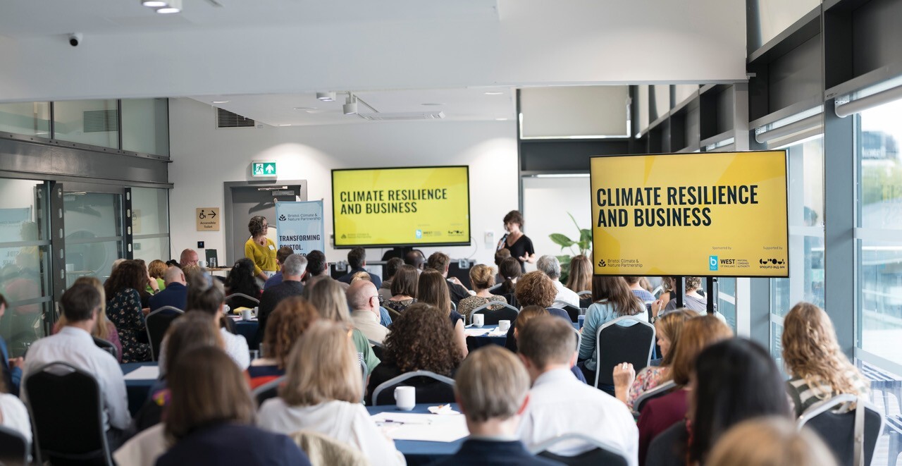 Attendees at a climate resilience event watching a presentation in a meeting room.