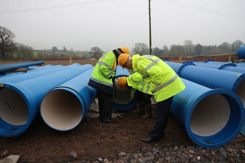 Three men in high visibility jackets and safety equipment surveying a large blue pipe