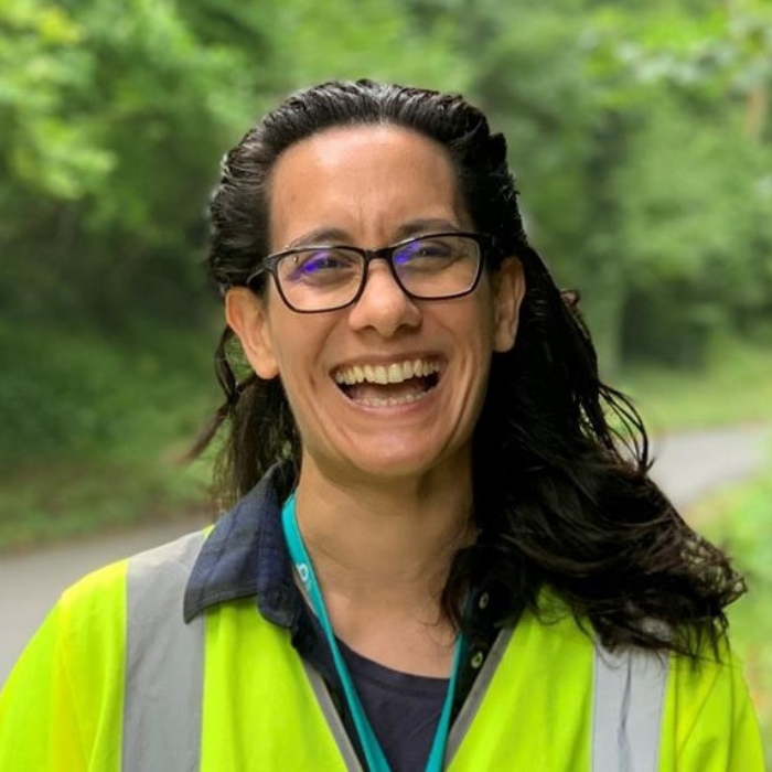 Natasha in a woody area, smiling with a high vis jacket on 