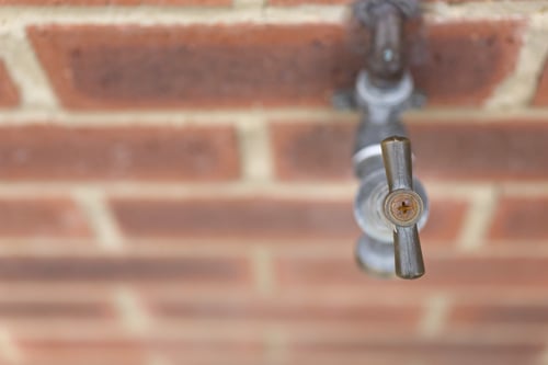 Detail of an outside tap on a red brick wall