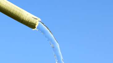 yellow hosepipe pouring water in front of blue sky