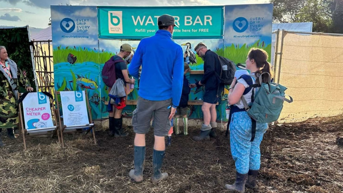 a couple standing in a field in front of the bristol water bar