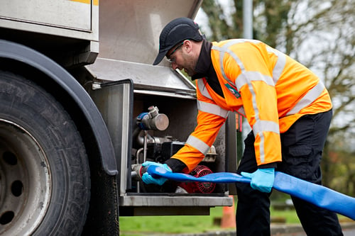A man in a high visibility jacket using a pipe to extract water from a water tanker lorry