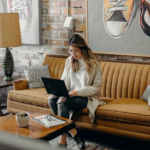 Woman using a laptop whilst sat on a sofa