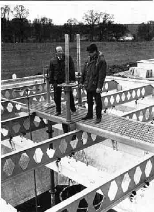 A black and white photo of two men standing above a water utility plant. 