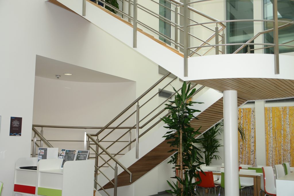 The lobby of the new Bristol Water offices. The walls are white and there are spiral stairs and large green plants in a light and airy lobby.