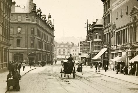 A sepia photo of Baldwin Street in Bristol. Shop fronts line the sides of the road and a horse and cart is heading down the middle of the street.