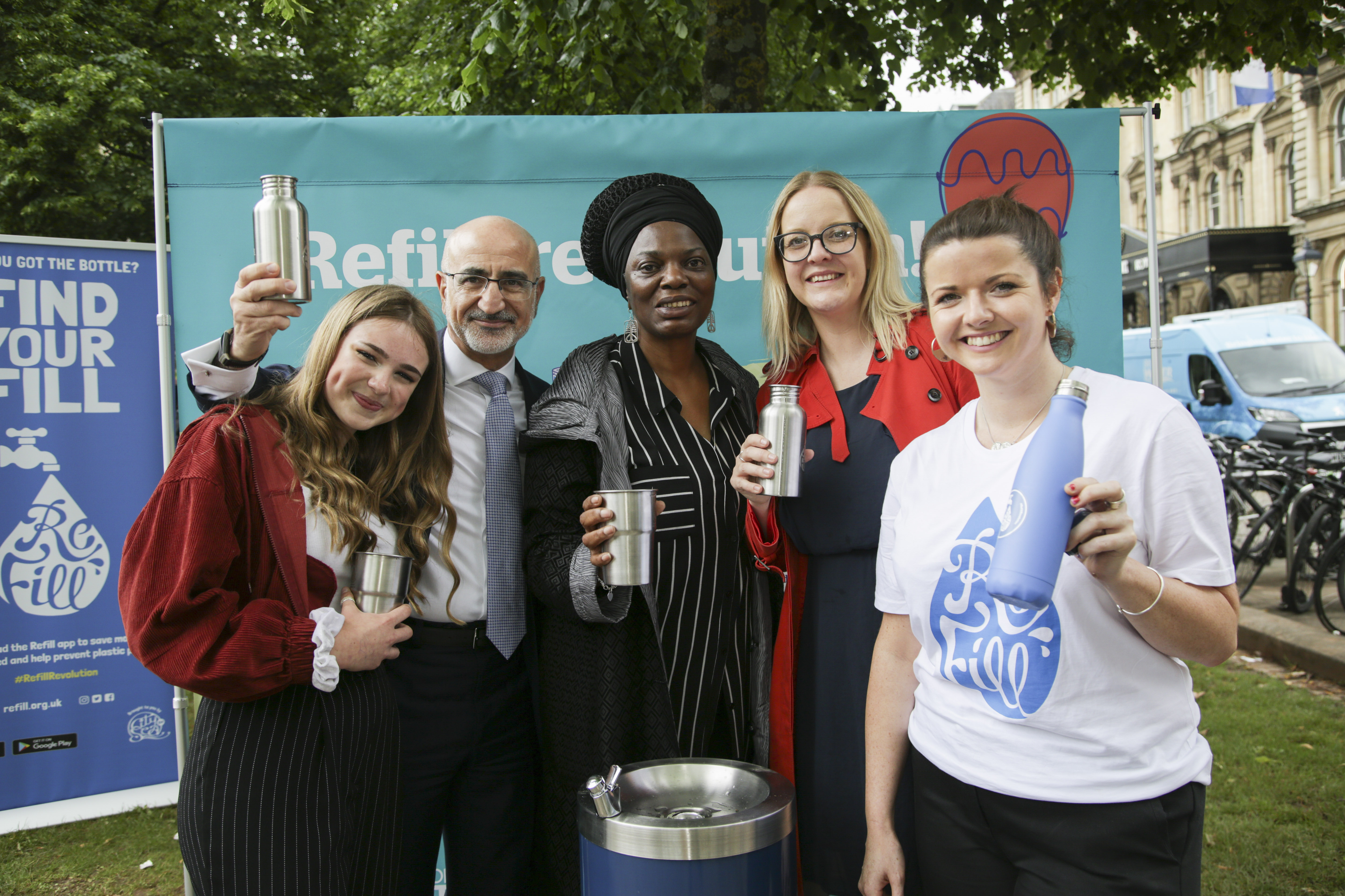 a group of people holding up refillable water bottles next to a Bristol Water fountain