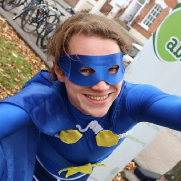 Mike in a dark blue superhero costume smiling at the camera in a field