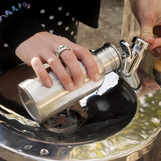 A person filling up a metal refillable water bottle from a water fountain