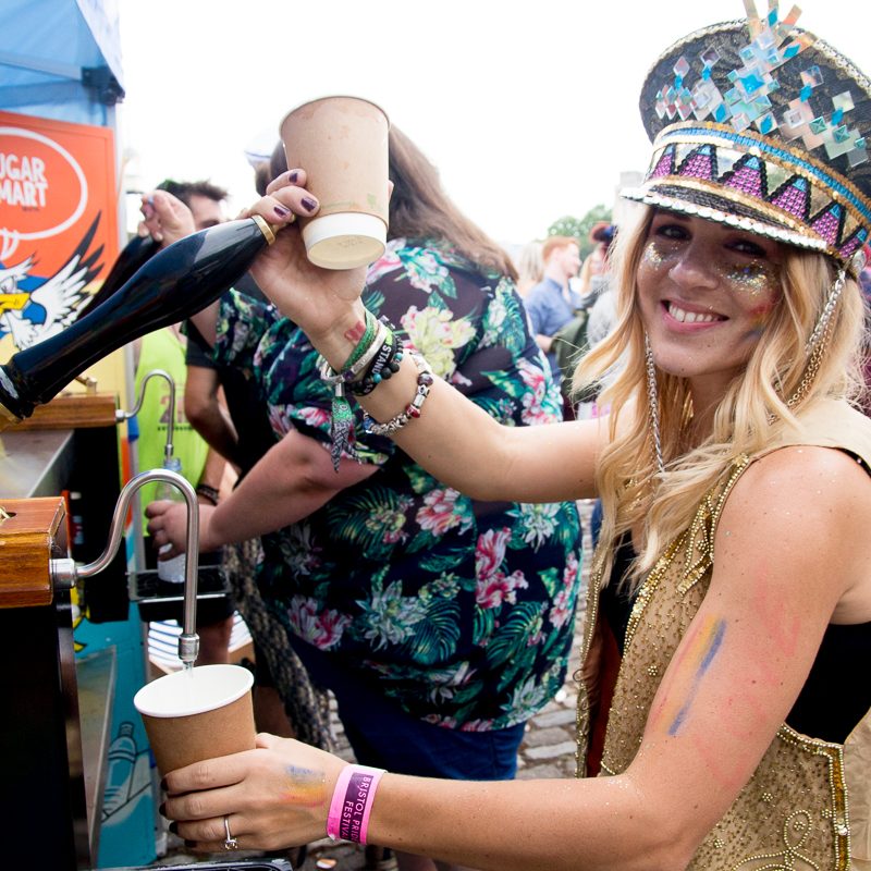 A smiling girl with a glittery hat filling up a cardboard cup with water from one of our free water bars