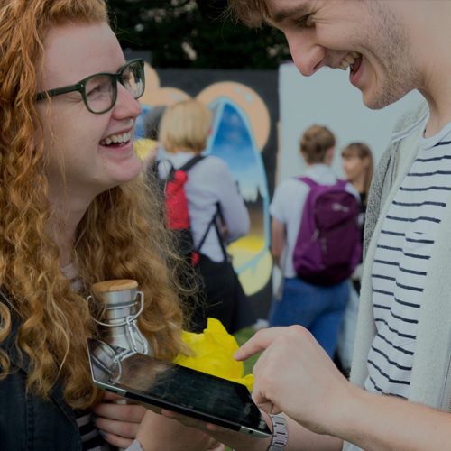 A girl smiling with a meta refillable water bottle talking to a man with an ipad